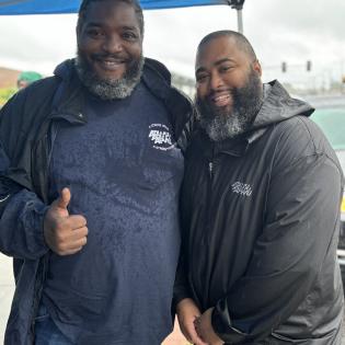 APWU members in Washington DC wearing blue shirts and gray rain jackets. One man on the left holds up a thumb 