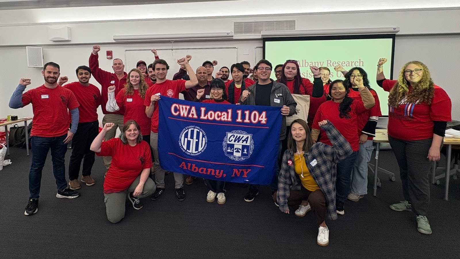 Workers pose for a group picture while holding signs.