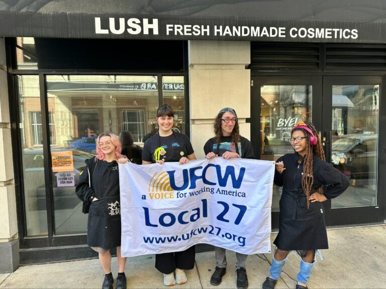 Lush workers pose for a group picture with a UFCW Local 27 banner.